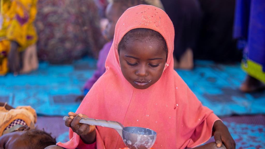 Una niña come  come gachas enriquecidas en un acto sobre nutrición de Plan Internacional.