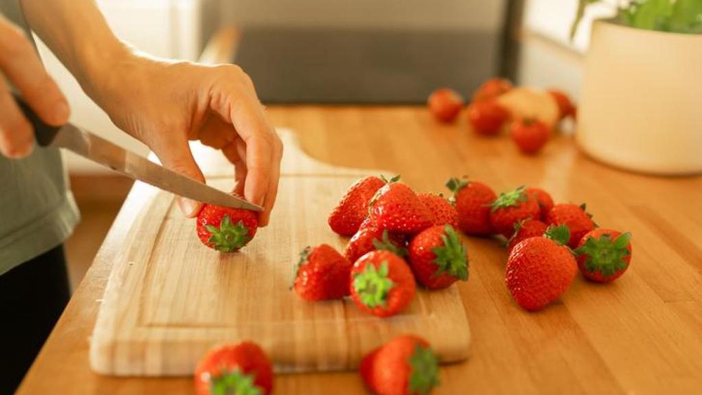 Mujer cortando fresas sobre una tabla.