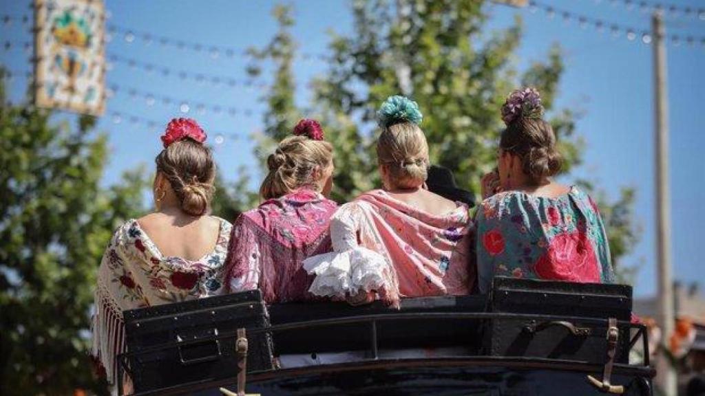 Imagen de varias mujeres montadas en un coche de caballos en la Feria de Sevilla.