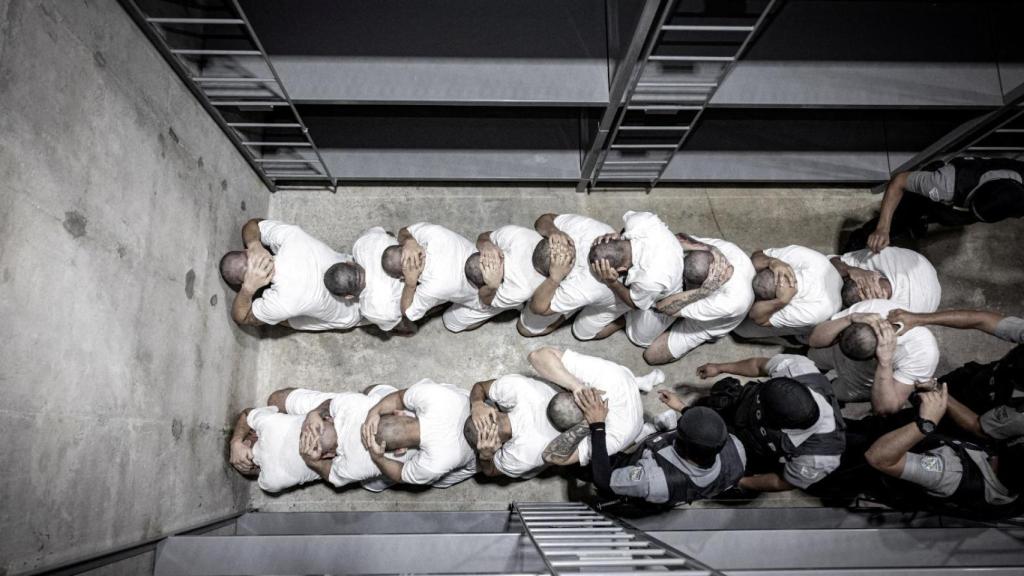 Policías salvadoreños escoltan a presuntos miembros de la pandilla venezolana Tren de Aragua, recientemente deportados por el gobierno estadounidense para ser encarcelados en el Centro de Reclusión del Terrorismo.