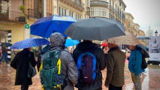 Un grupo de personas bajo la lluvia en la plaza de la Constitución de Málaga.