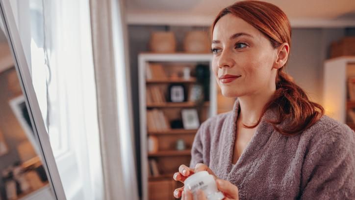 Mujer en albornoz echándose crema facial.