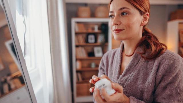 Mujer en albornoz echándose crema facial.