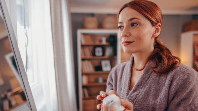 Mujer en albornoz echándose crema facial.