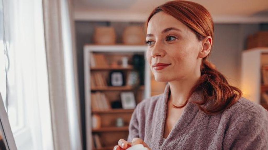 Mujer en albornoz echándose crema facial.