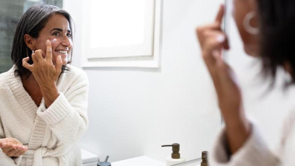 Mujer en albornoz aplicándose crema en el rostro.
