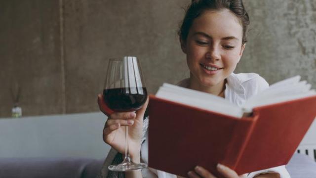 Mujer bebiendo vino tinto mientras lee.