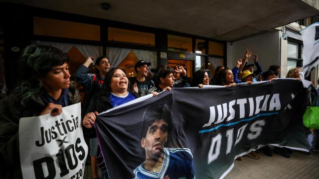 Fanáticos de Diego Armando Maradona sostienen una pancarta que dice Justicia para Dios a las puertas del juzgado.