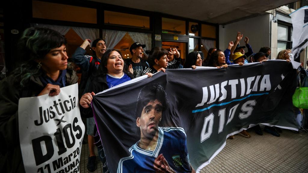 Fanáticos de Diego Armando Maradona sostienen una pancarta que dice Justicia para Dios a las puertas del juzgado