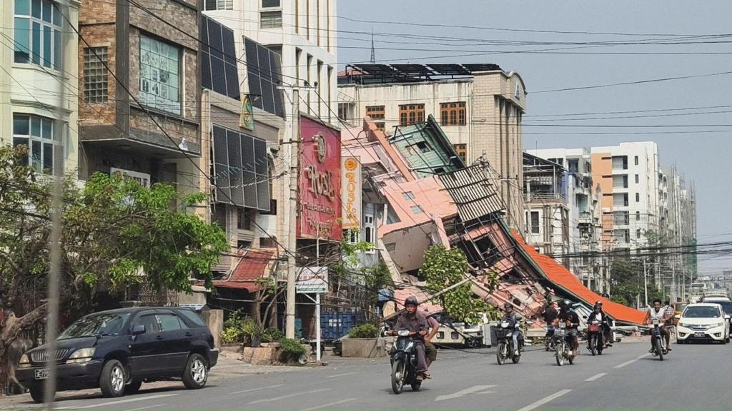 La gente pasa en motocicleta junto a un edificio dañado después de que un fuerte terremoto azotara el centro de Myanmar, en Mandalay.