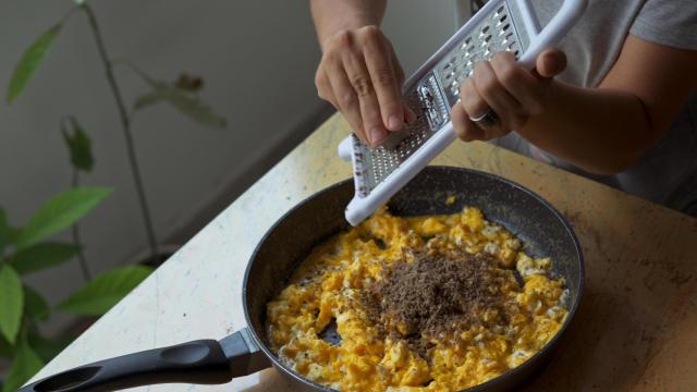 Una mujer ralla trufa sobre un revuelto de tortilla.