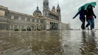 Dos personas se resguardan de la lluvia frente al Palacio Real de Madrid.