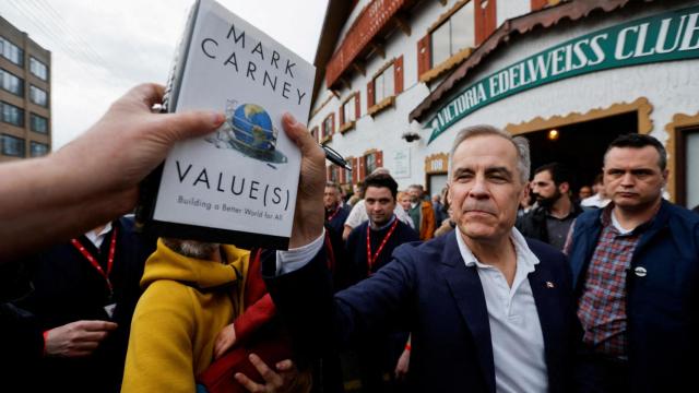 El primer ministro de Canadá, Mark Carney, coge un libro de un simpatizante para autografiarlo fuera del Victoria Edelweiss Club, durante su gira de campaña electoral del Partido Liberal en Victoria, Columbia Británica, Canadá 6 de abril de 2025.
