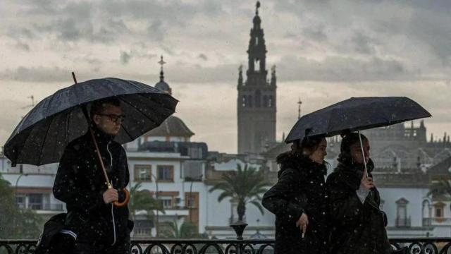 Un grupo de personas camina con paraguas bajo la lluvia por el Puente de Triana, en Sevilla. (Archivo)