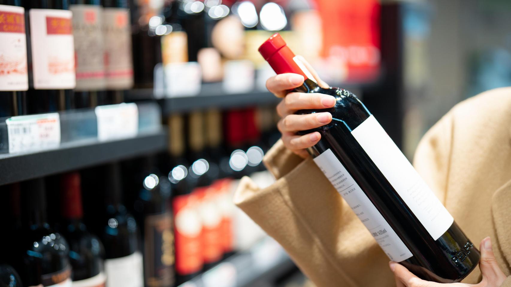 Una persona escogiendo un vino en un supermercado.