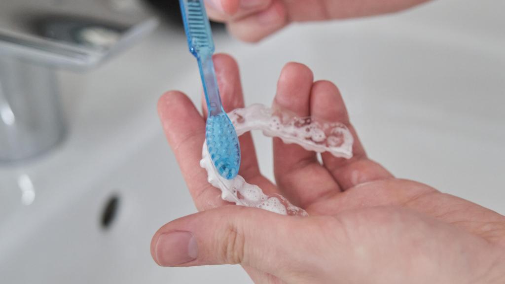 Una mano limpiando un alineador dental transparente.