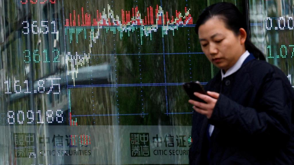 Una mujer pasa frente a una casa de bolsa con un panel con información del índice bursátil, en Pekín.