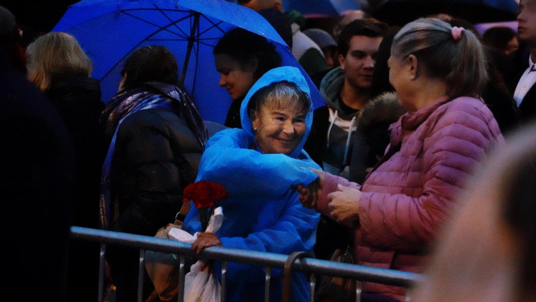 Una señora, claveles en mano, con su chubasquero.