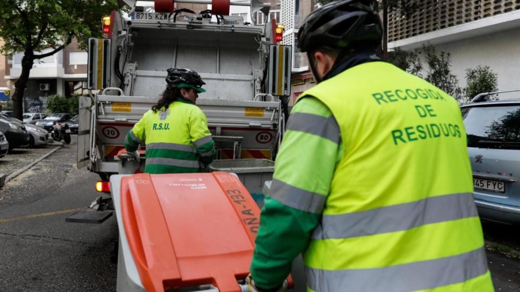 Dos operarios de recogida de residuos trasladan cubos de basura en una calle de Madrid.
