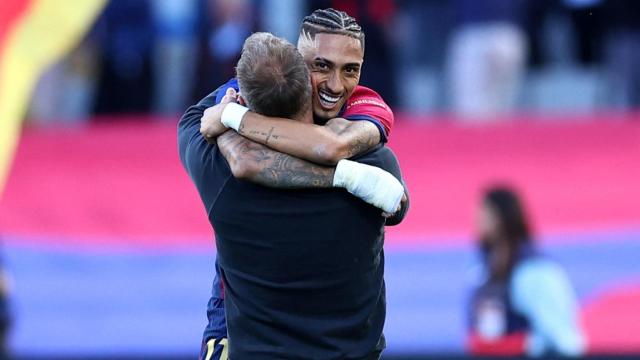 Raphinha y Hansi Flick se abrazan.