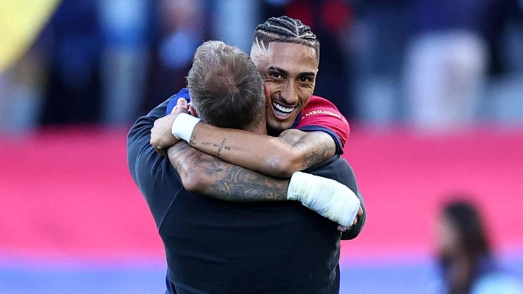 Raphinha y Hansi Flick se abrazan.