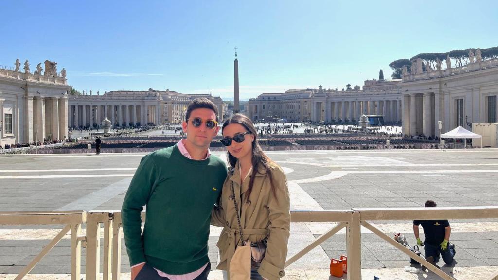 Ana y su pareja en las puertas de la basílica de San Pedro, mientras operarios trabajan en los preparativos de la capilla ardiente. EE