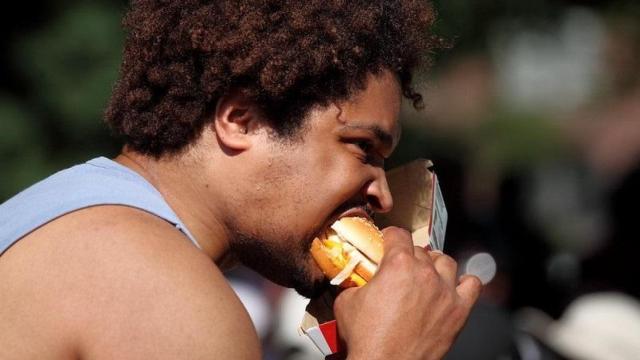 Hombre comiendo una hamburguesa en la calle.