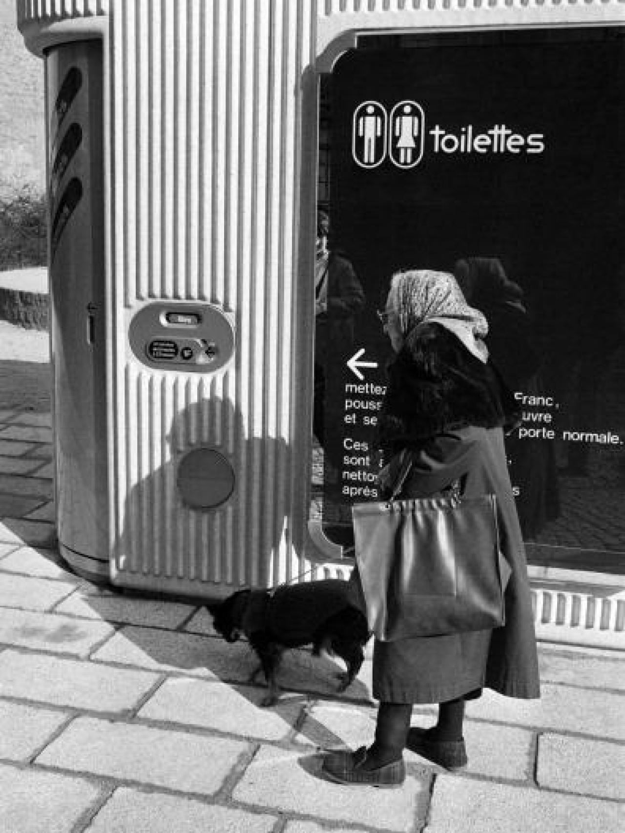 Mujer paseando al lado de un baño público para hombres y mujeres.