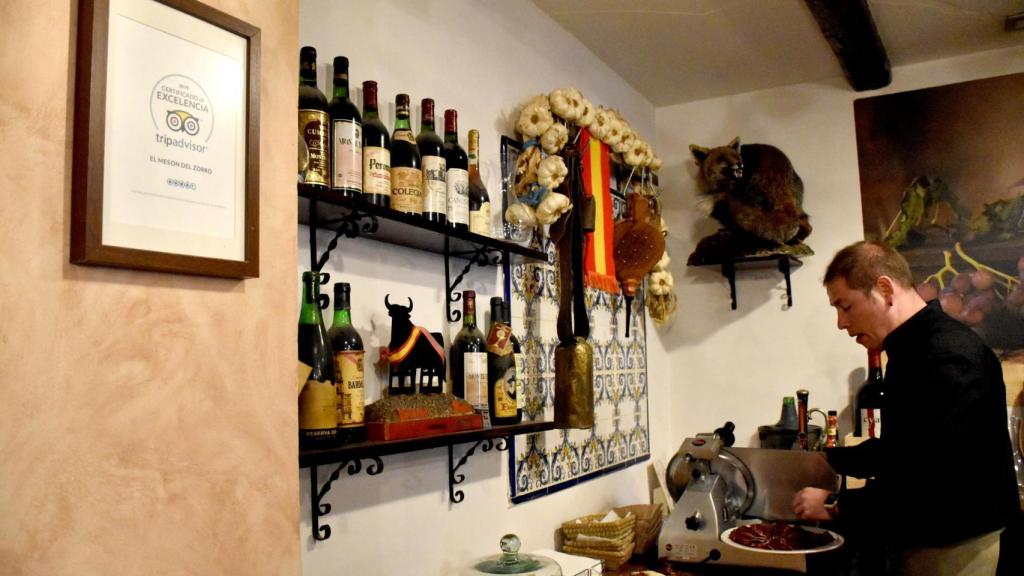Javier prepara un plato de embutido y en la pared de al lado cuelga el título de excelencia de TripAdvisor