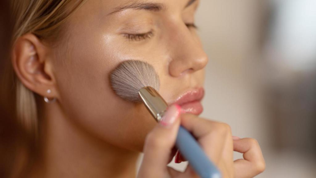 Mujer aplicándose maquillaje con una brocha.