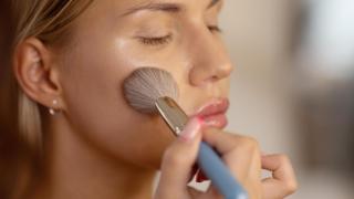 Mujer aplicándose maquillaje con una brocha.