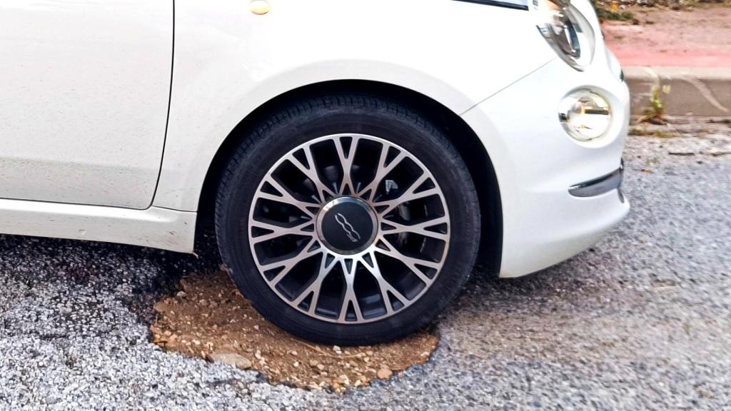 Un coche mete la rueda en un bache de la carretera.