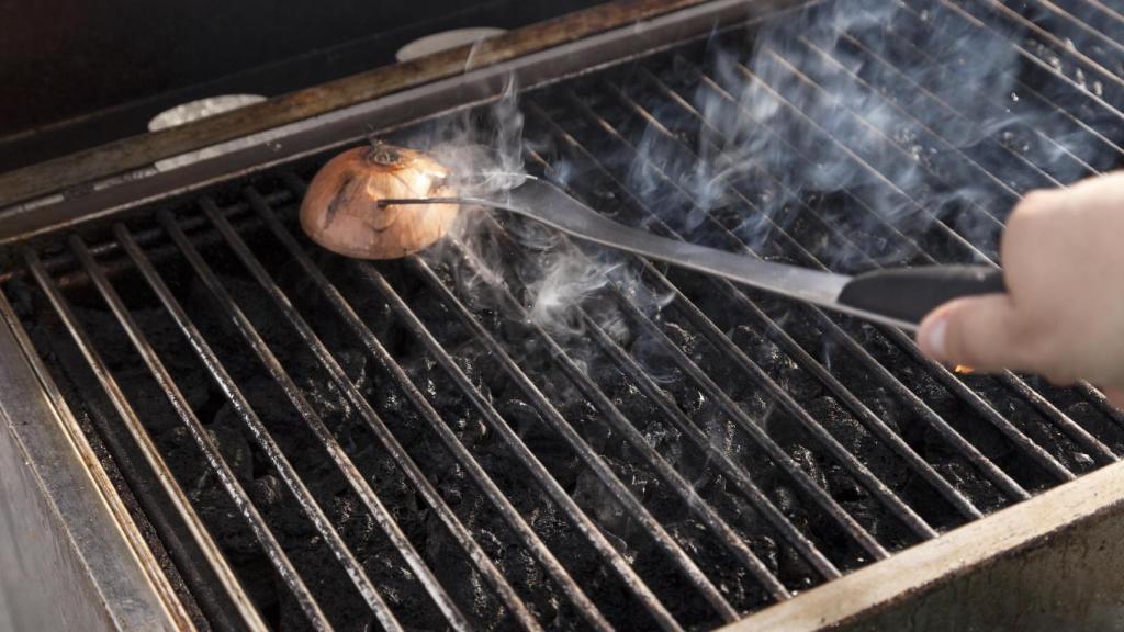 Una persona frotando una parrilla con media cebolla