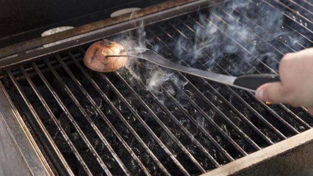 Una persona frotando una parrilla con media cebolla
