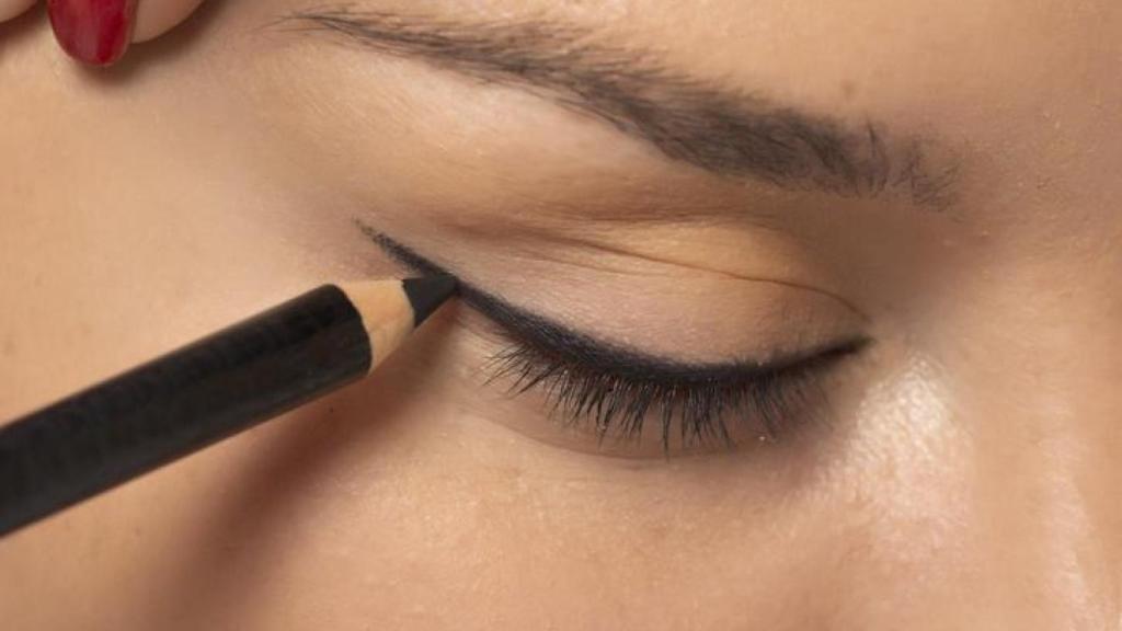 Mujer aplicándose lápiz de ojos.