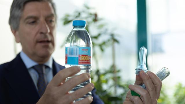 Vicente Montojo, Regional Director de Plastipak, sostiene con su mano izquierda una preforma, producto intermedio de plástico que tras un proceso de soplado se convertirá en la botella de agua 100% reciclada que sostiene con la derecha.