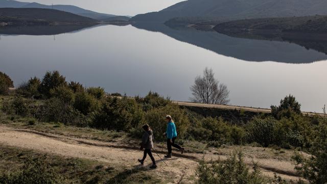 Dos personas haciendo senderismo a orillas de un embalse.