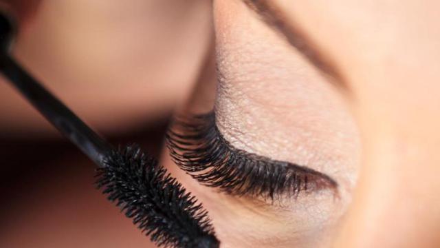 Mujer aplicándose máscara de pestañas.