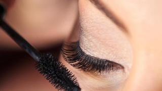 Mujer aplicándose máscara de pestañas.