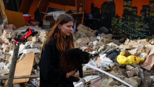 Una vecina carga a su gato entre los restos de una casa atacada por drones rusos en Kyiv.