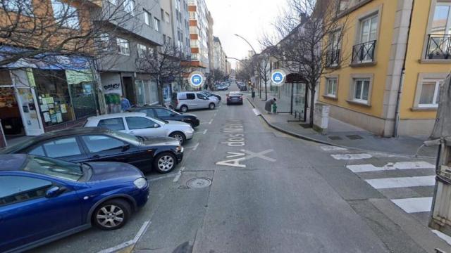 Tramo de la avenida de Os Mallos por el que pasa el bus, con vehículos aparcados en batería delante de la parada.