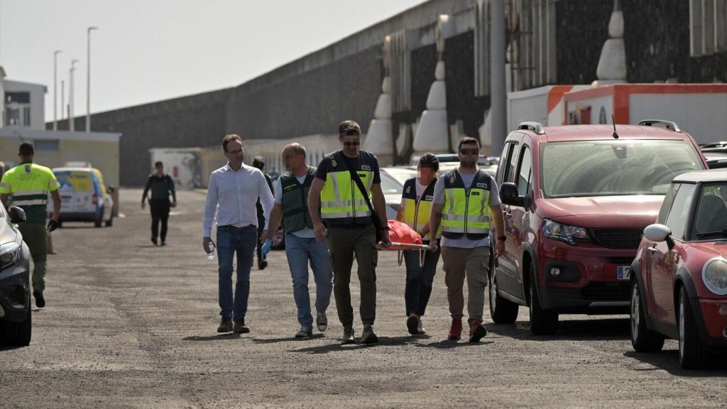 Agentes de Policía Nacional y Guardia Civil llevan en la camilla a rescatan a uno de los migrantes que viajaban en el cayuco que ha volcado a su llegada al puerto de La Restinga.