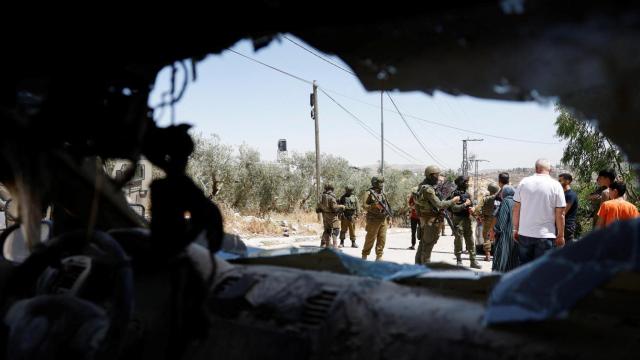 Soldados israelíes hacen guardia cerca de un coche dañado tras el ataque de colonos israelíes en Qaryout, cerca de Nablus, en la Cisjordania ocupada.