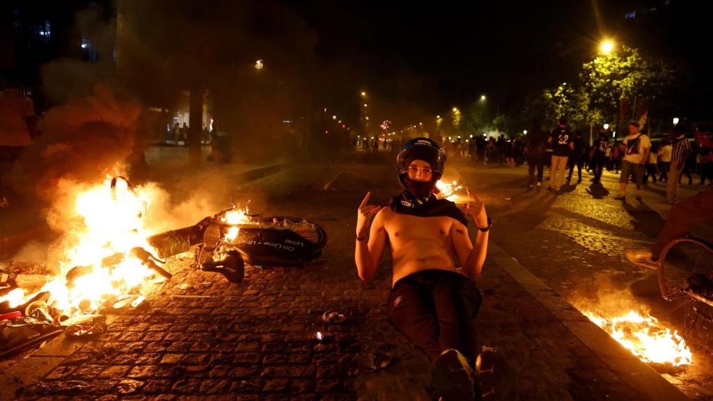 Un seguidor del PSG posa junto a una bicicleta en llamas, la los Campos Elíseos de París.