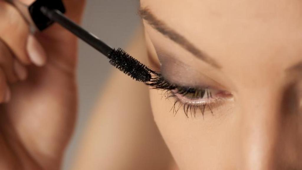 Mujer aplicándose máscara de pestañas.