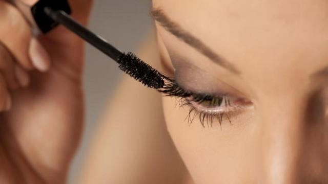 Mujer aplicándose máscara de pestañas.