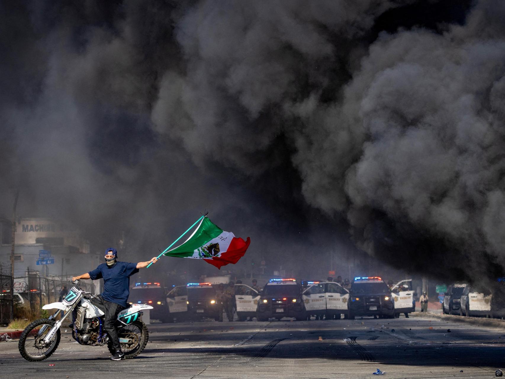 Un manifestante enarbola la bandera mexicana frente a una línea de policías durante las protestas contra las redadas del Servicio de Inmigración y Control de Aduanas (ICE) en Los Ángeles.