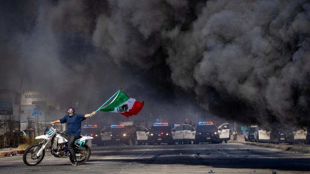 Un manifestante enarbola la bandera mexicana frente a una línea de policías durante las protestas contra las redadas del Servicio de Inmigración y Control de Aduanas (ICE) en Los Ángeles.