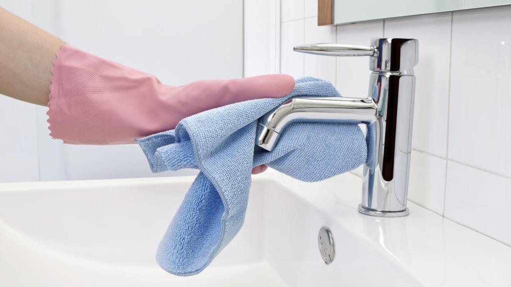Manos con guantes limpiando un grifo de baño.