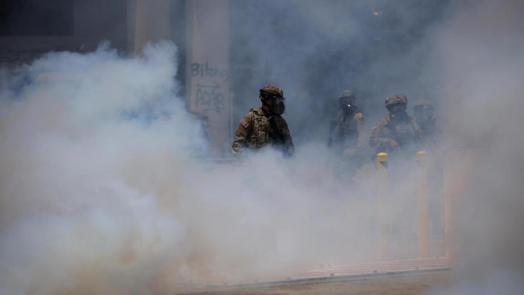 El humo se eleva mientras miembros de la Guardia Nacional de California se reúnen durante una protesta contra las redadas federales de inmigración en el centro de Los Ángeles,